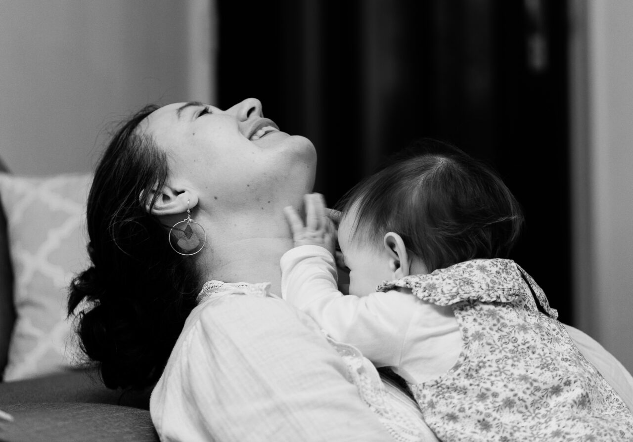 Photo d'une maman et de son bébé. Ils rigolent tous les deux. Moment de joie et connivence. Photo noir et blanc.